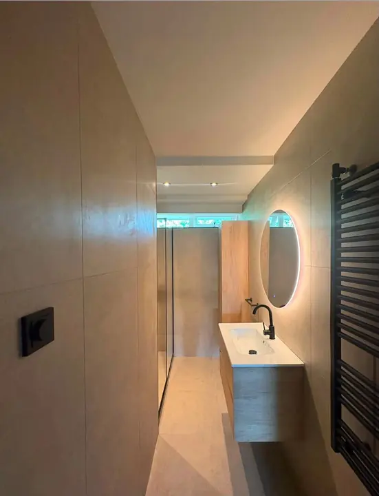Opgeleverde badkamer in Nijmegen met inloopdouche, zwevend wastafelmeubel en ronde spiegel met verlichting