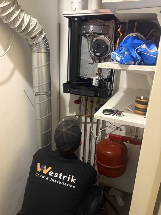 Monteur van Westrik Bouw & Installaties werkt aan het leidingwerk onder een Intergas CW4 in een kast in Nijmegen, met de mantel van het toestel eraf