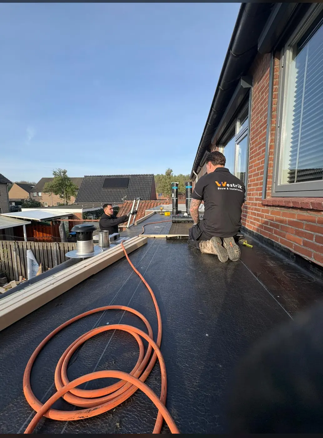 Twee monteurs van Westrik leggen nieuwe bitumen dakbedekking op een plat dak in Nijmegen, rond roestvrijstalen dakdoorvoeren