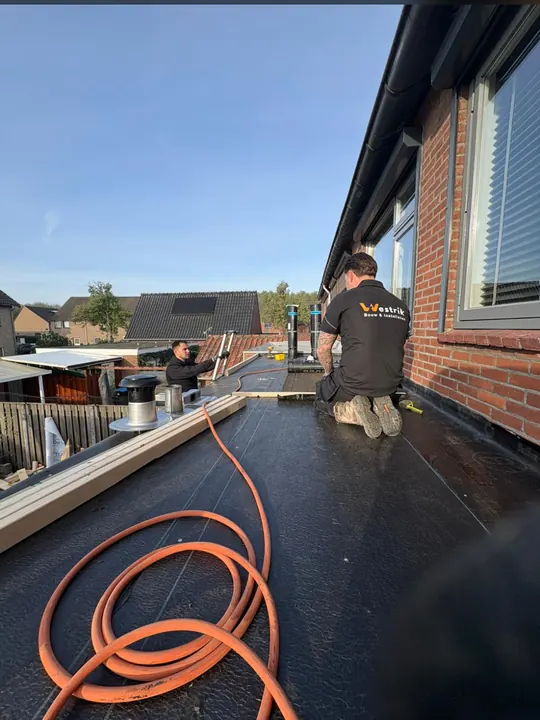 Twee monteurs van Westrik leggen nieuwe bitumen dakbedekking op een plat dak in Nijmegen, rond roestvrijstalen dakdoorvoeren