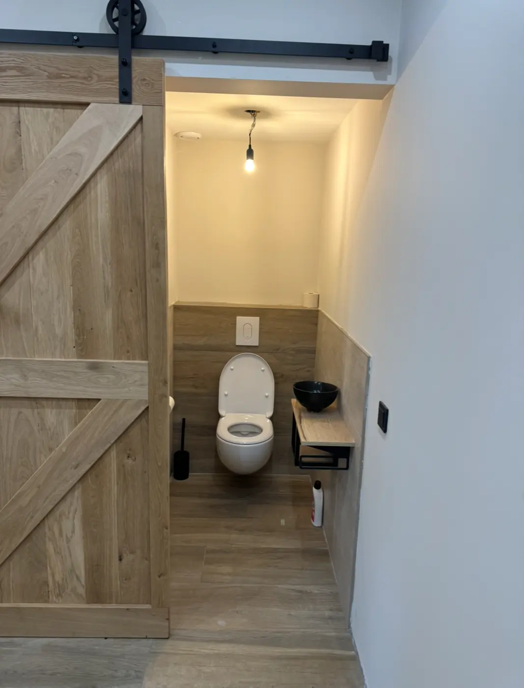 Gerenoveerd toilet in Nijmegen met een eiken schuifdeur op een zwarte stalen rail, houtlook tegelwerk en een hangtoilet
