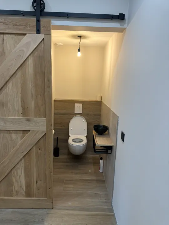 Gerenoveerd toilet in Nijmegen met een eiken schuifdeur op een zwarte stalen rail, houtlook tegelwerk en een hangtoilet