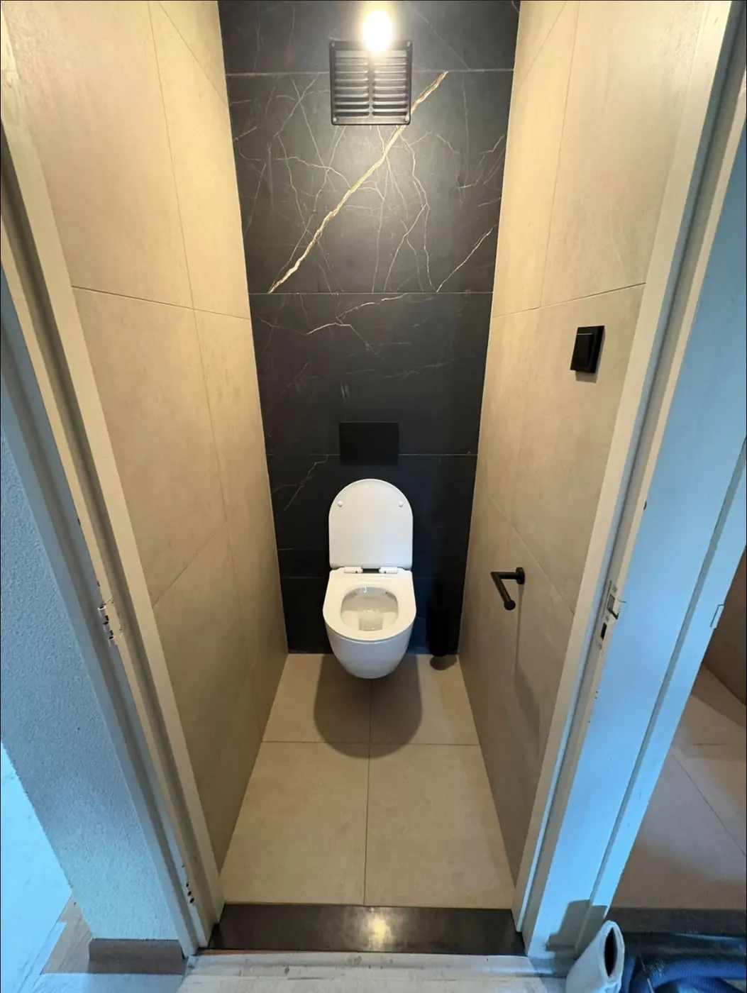 Gerenoveerd toilet in Nijmegen met hangend toilet, donkere accentwand en zwarte bedieningsplaat
