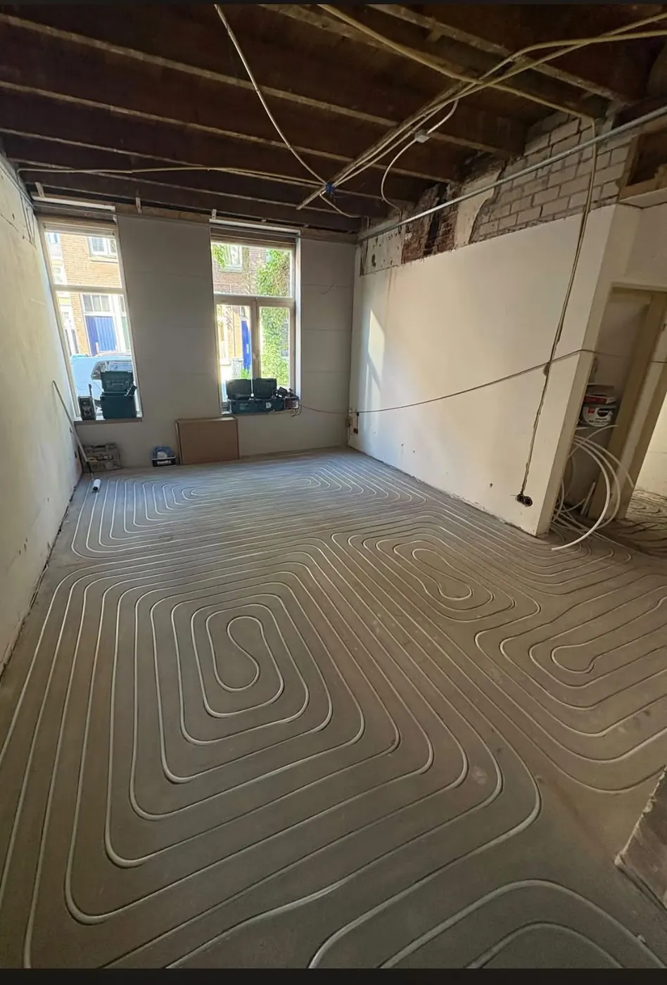 Vloerverwarmingsleidingen in een gestripte woonkamer in Nijmegen, klaar voor de dekvloer